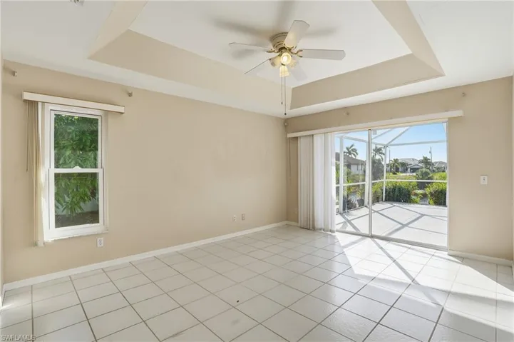 Empty room with a raised ceiling, ceiling fan, and healthy amount of natural light