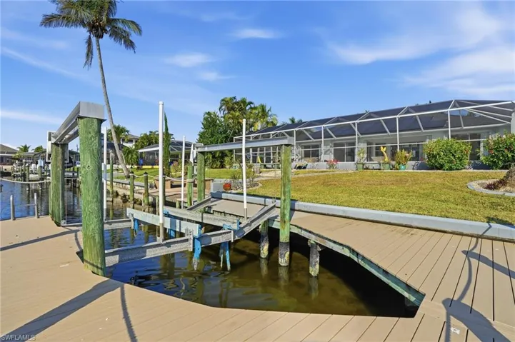 Dock area with boat lift, a sunroom, a water view, a lawn, and glass enclosure