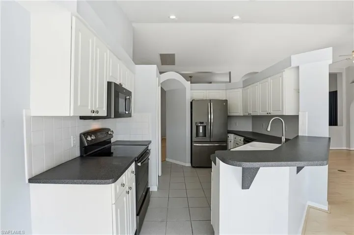 Kitchen with dark countertops, black / electric stove, stainless steel fridge, a peninsula, and tasteful backsplash