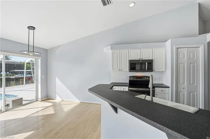 Kitchen featuring stainless steel appliances, lofted ceiling, tasteful backsplash, decorative light fixtures, and white cabinets