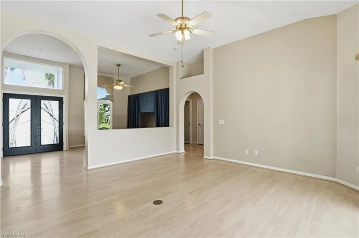 Unfurnished living room with arched walkways, a ceiling fan, light wood finished floors, a high ceiling, and french doors