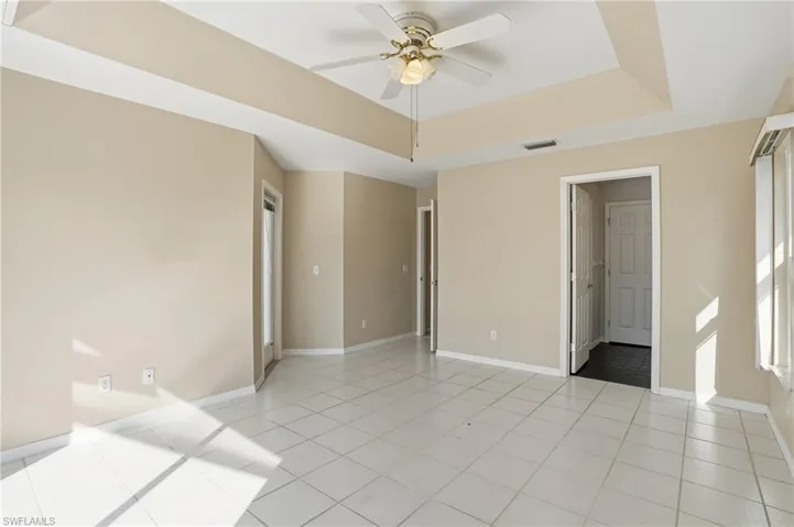 Unfurnished bedroom featuring a raised ceiling, a ceiling fan, and light tile patterned flooring