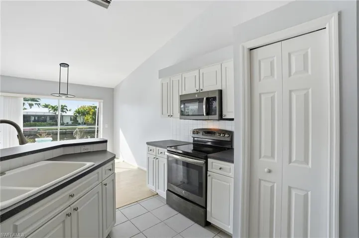 Kitchen featuring appliances with stainless steel finishes, dark countertops, white cabinetry, and lofted ceiling