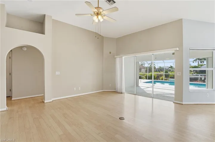 Spare room featuring a high ceiling, a ceiling fan, arched walkways, and light wood-style flooring