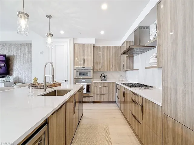 Kitchen featuring wall chimney exhaust hood, hanging light fixtures, stainless steel appliances, sink, and light wood-type flooring