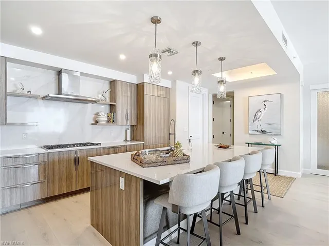 Kitchen with stainless steel gas stovetop, a kitchen island with sink, light hardwood / wood-style flooring, pendant lighting, and ventilation hood