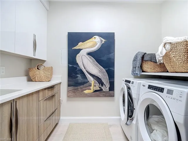 Clothes washing area with cabinets, washing machine and clothes dryer, and light hardwood / wood-style floors