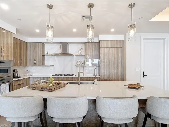 Kitchen with wall chimney range hood, hanging light fixtures, backsplash, and a large island