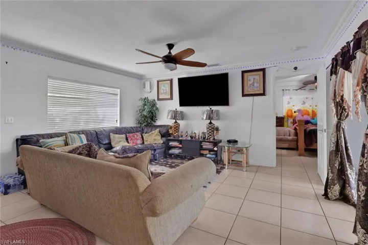 Living room featuring a ceiling fan, light tile patterned floors, and crown molding