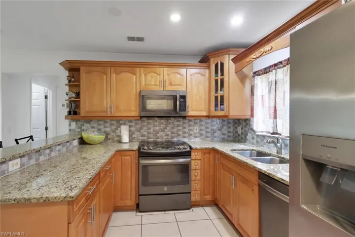 Kitchen featuring stainless steel appliances, light stone counters, a peninsula, light tile patterned flooring, and decorative backsplash