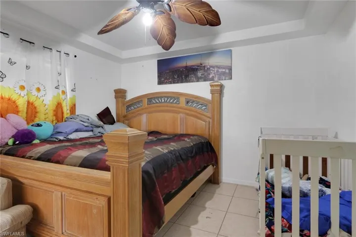 Bedroom with light tile patterned floors, a ceiling fan, and a tray ceiling