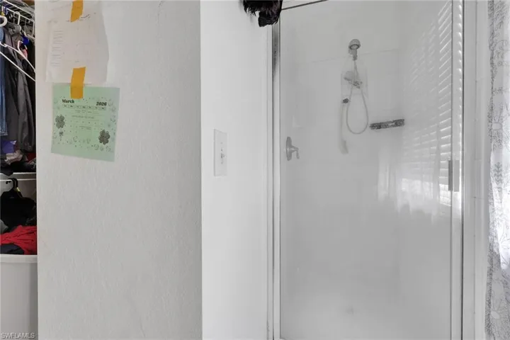 Bathroom featuring a shower stall, a textured wall, and a walk in closet