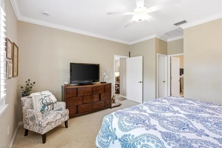 Interior room featuring crown molding, neutral wall tones, carpeted flooring, a ceiling fan with integrated lighting, and multiple interior doorways