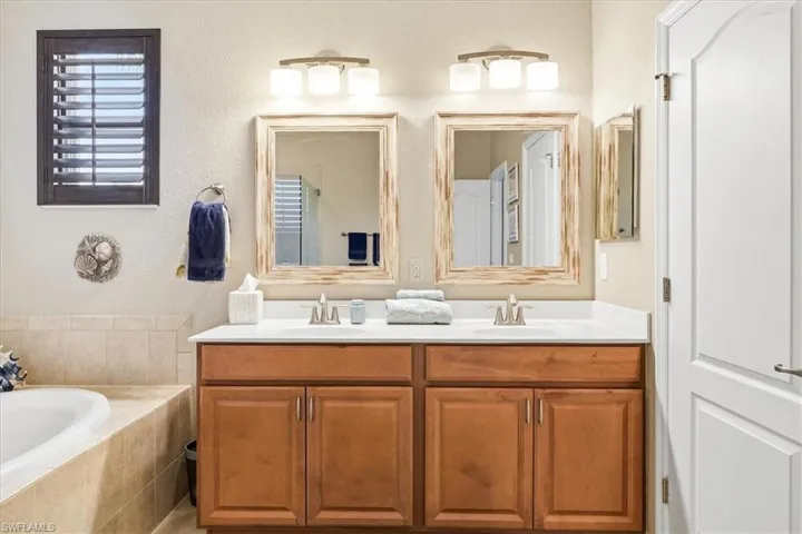 Dual wood-finish vanities with white countertops and undermount sinks, illuminated by individual three-light fixtures