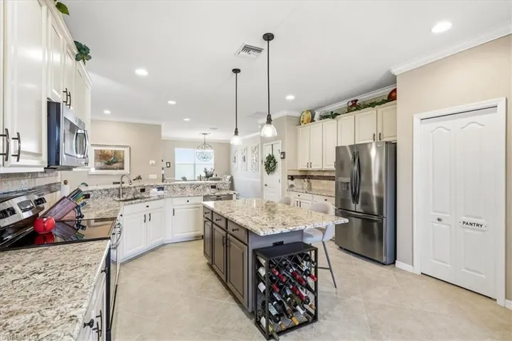 Spacious kitchen featuring light-toned cabinetry, stainless steel appliances, granite countertops, tile flooring, and a central island with pendant lighting