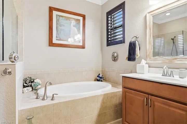 Built-in soaking tub with tile surround, wood-finish vanity with single sink, framed mirror, and a glass-enclosed shower
