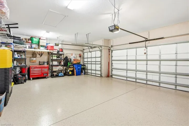 Spacious garage featuring a light-toned, speckled epoxy floor, two overhead garage doors, and built-in shelving