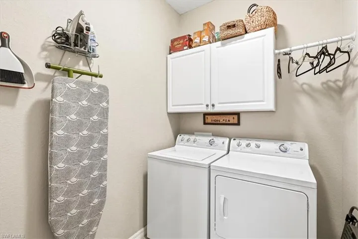 Dedicated utility space featuring a washer and dryer, upper cabinetry, and a wall-mounted drying rack