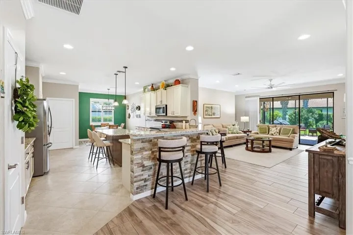Open concept living area featuring a kitchen island with stone veneer detailing and pendant lighting, wood-finish flooring, recessed lighting, and sliding glass doors