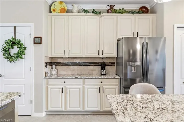 Kitchen featuring cream cabinetry with black hardware, a stainless steel French door refrigerator, speckled granite countertops, and a tiled backsplash with decorative accents