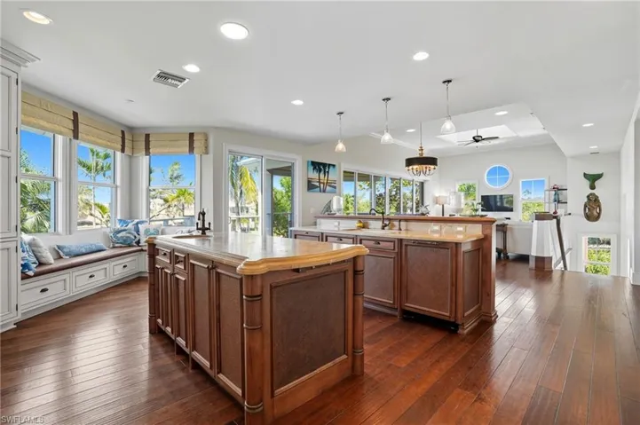 Kitchen featuring open floor plan, recessed lighting, decorative light fixtures, brown cabinetry, and light stone counters - Virtually Edited Image