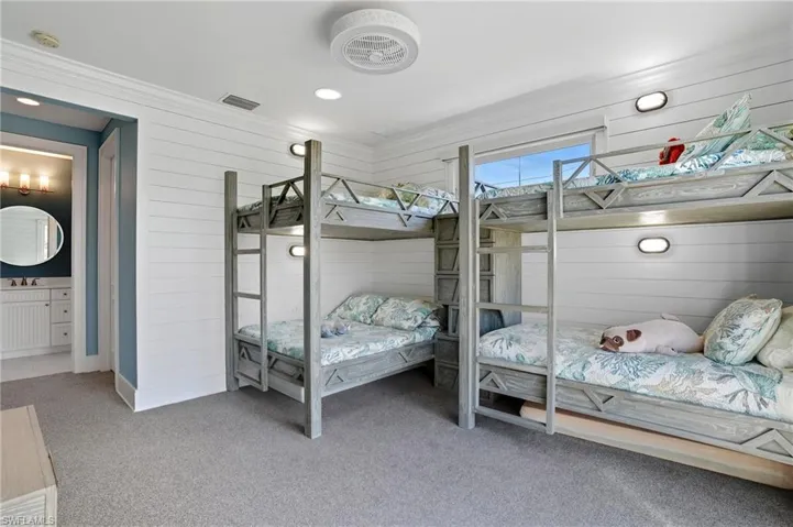 Bedroom featuring wood walls, light carpet, ornamental molding, recessed lighting, and connected bathroom - Virtually Edited Image