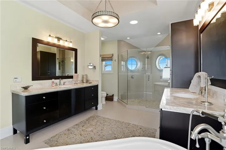 Bathroom featuring a stall shower, two vanities, light tile patterned floors, and recessed lighting - Virtually Edited Image
