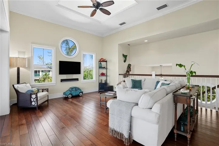 Living room featuring ornamental molding, ceiling fan, and dark wood-type flooring - Virtually Edited Image