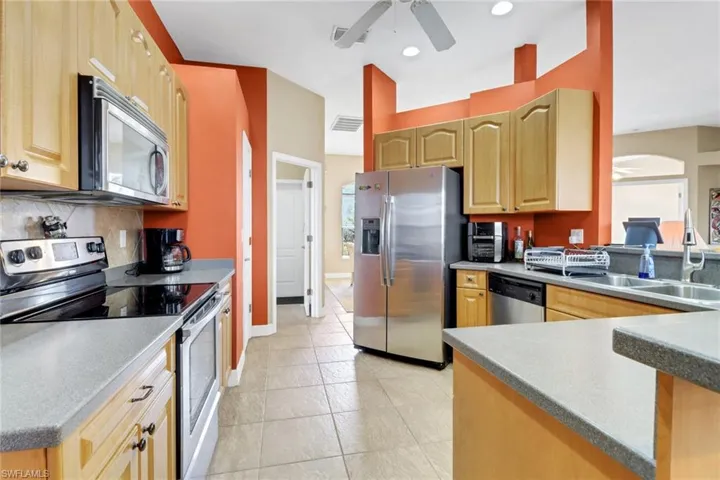 Kitchen featuring appliances with stainless steel finishes, ceiling fan, tasteful backsplash, light brown cabinetry, and arched walkways