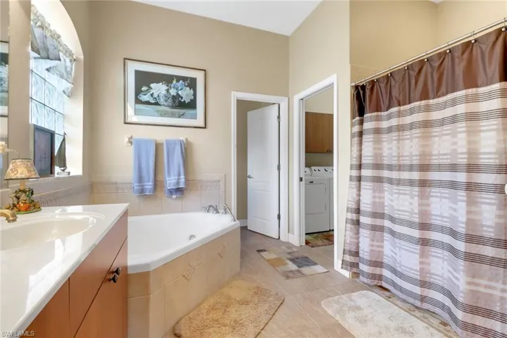 Bathroom featuring vanity, washer and dryer, a garden tub, tile patterned floors, and curtained shower