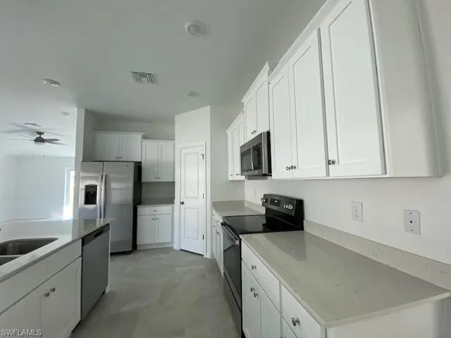 Kitchen featuring stainless steel appliances, white cabinetry, a ceiling fan, and light stone counters