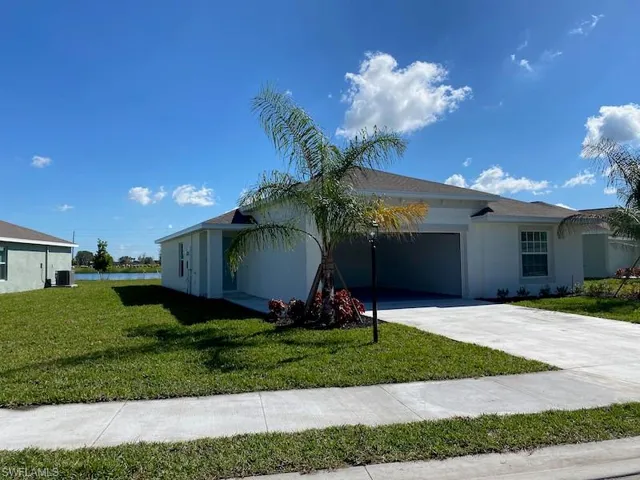 Ranch-style house featuring an attached garage, a front yard, stucco siding, and driveway