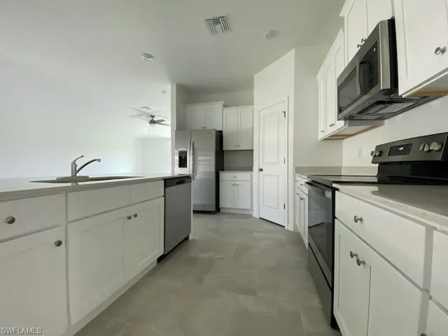 Kitchen with stainless steel appliances, white cabinetry, light stone counters, and a ceiling fan