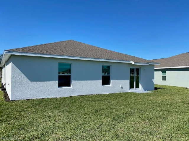Back of house featuring a lawn, stucco siding, and roof with shingles