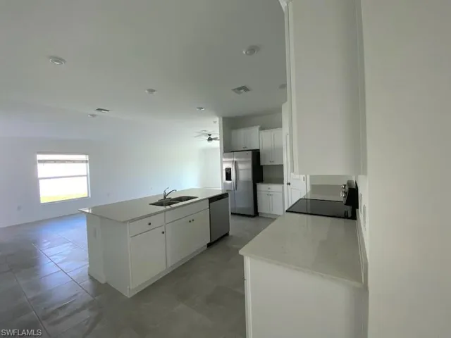 Kitchen with an island with sink, stainless steel appliances, white cabinetry, light stone countertops, and open floor plan