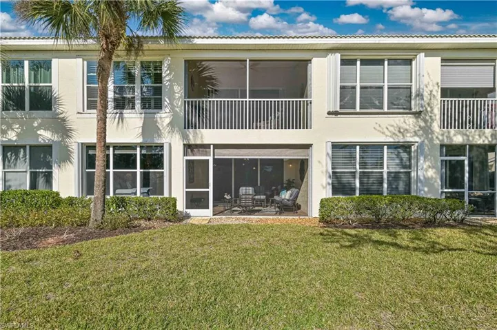 Back of house featuring a balcony, stucco siding, a sunroom, and a lawn