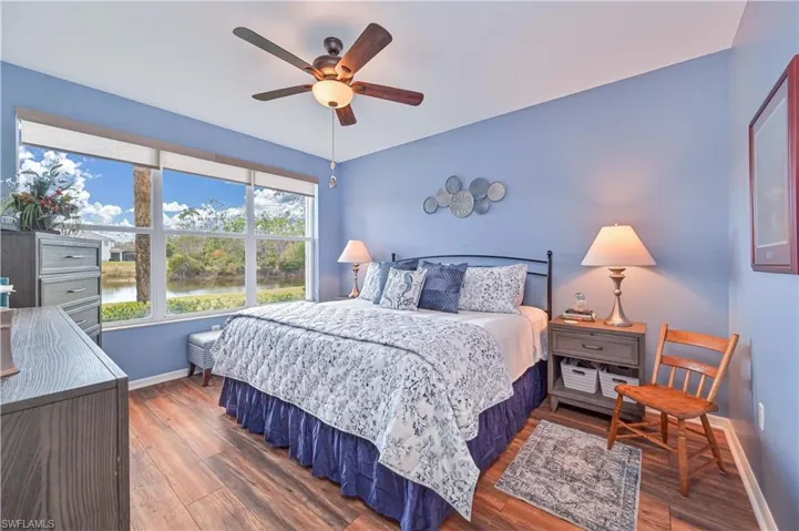 Bedroom with a water view, dark wood finished floors, and a ceiling fan