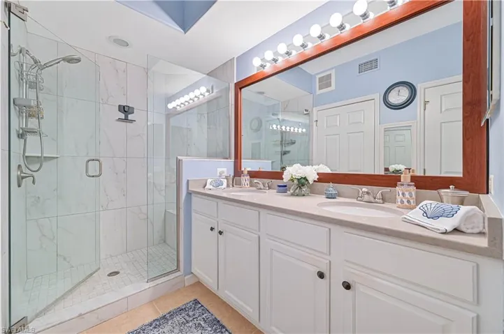 Bathroom featuring double vanity, a marble finish shower, and light tile patterned floors