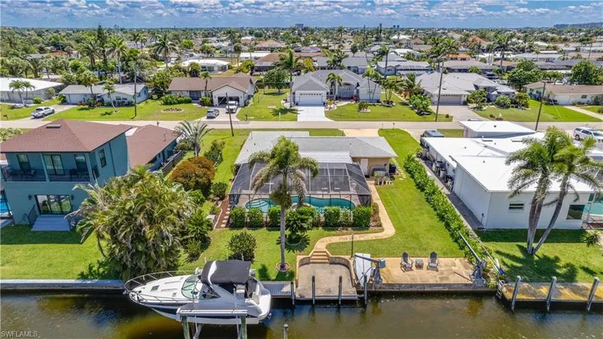 Back of house showing a tropical caged pool, lush tropical landscaping, and a dock with boat lift on a River/Gulf access canal.