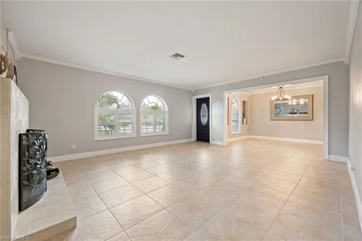 Unfurnished living room with ornamental molding, light tile patterned flooring, a fireplace, and a chandelier
