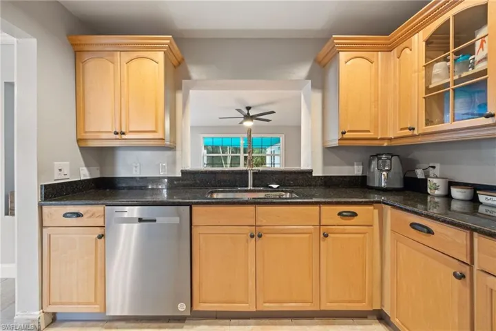 Kitchen featuring dishwasher, dark stone counters, glass insert cabinets, and light brown cabinetry