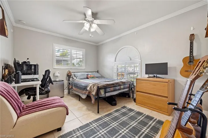 Bedroom with ornamental molding, an office area, multiple windows, light tile patterned flooring, and a ceiling fan