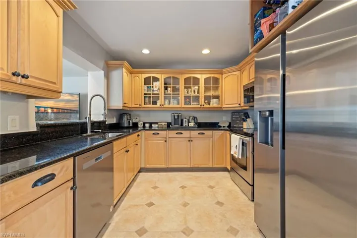 Kitchen with appliances with stainless steel finishes, dark stone counters, glass insert cabinets, light brown cabinets, and recessed lighting