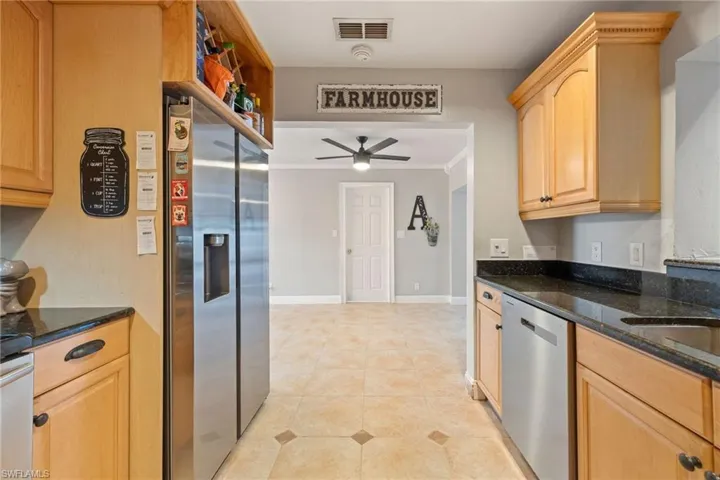 Kitchen with dark stone counters, appliances with stainless steel finishes, a ceiling fan, and light brown cabinetry