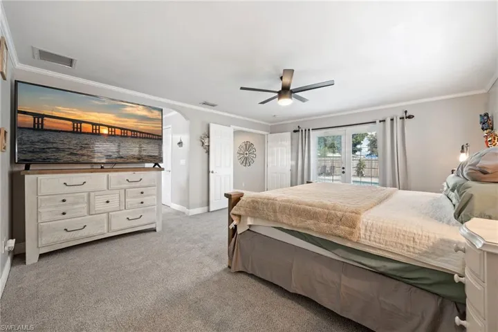 Bedroom featuring light colored carpet, crown molding, ceiling fan, access to exterior, and arched walkways