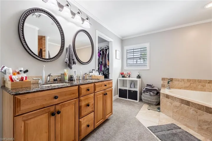 Full bathroom with double vanity, ornamental molding, and a bath