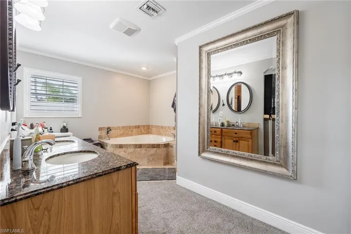 Bathroom with a bath, double vanity, and crown molding