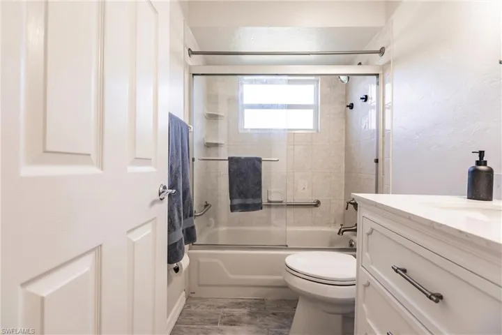 Full bathroom with bath / shower combo with glass door, tile patterned floors, vanity, and toilet