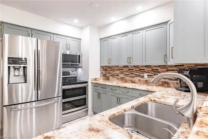 Kitchen featuring stainless steel appliances, decorative backsplash, sink, and light stone counters