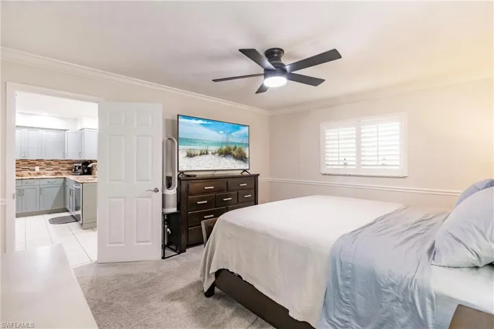 Bedroom with ceiling fan, light colored carpet, ensuite bath, and ornamental molding